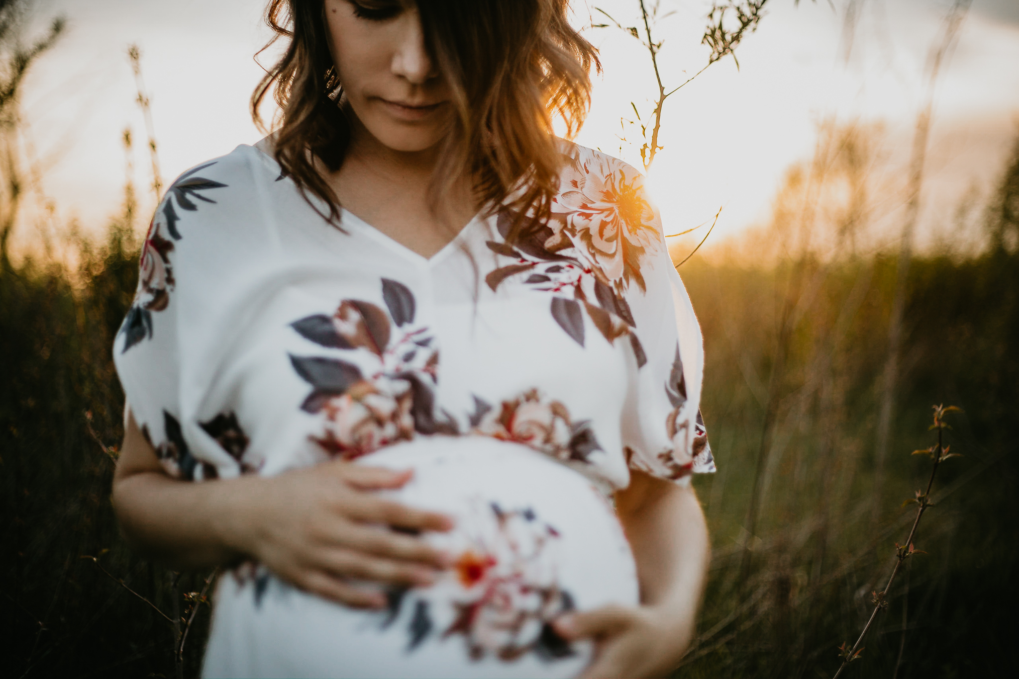 Pregnant mother at golden hour looking down at her belly.